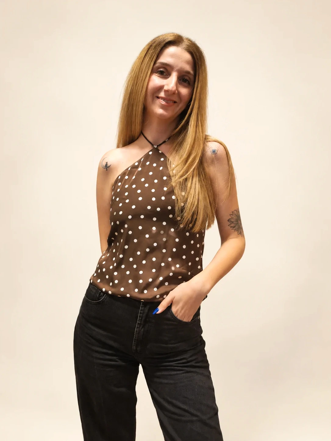 Aleksandra standing against a white wall in a polka-dot halter top and black jeans